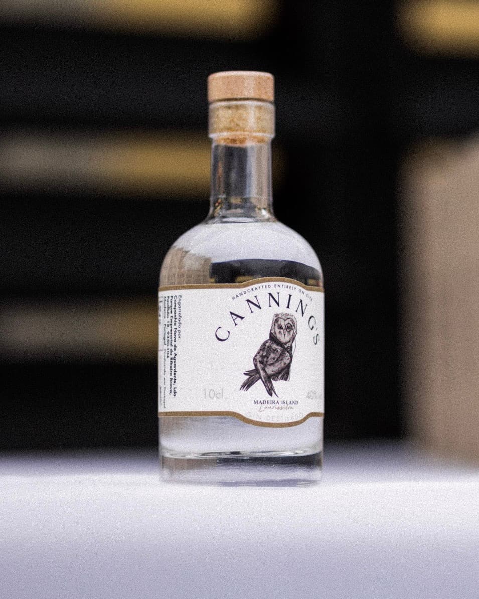 Seis garrafas de 10cl de gin Canning's na bancada da destilaria, com o alambique de cobre atrás