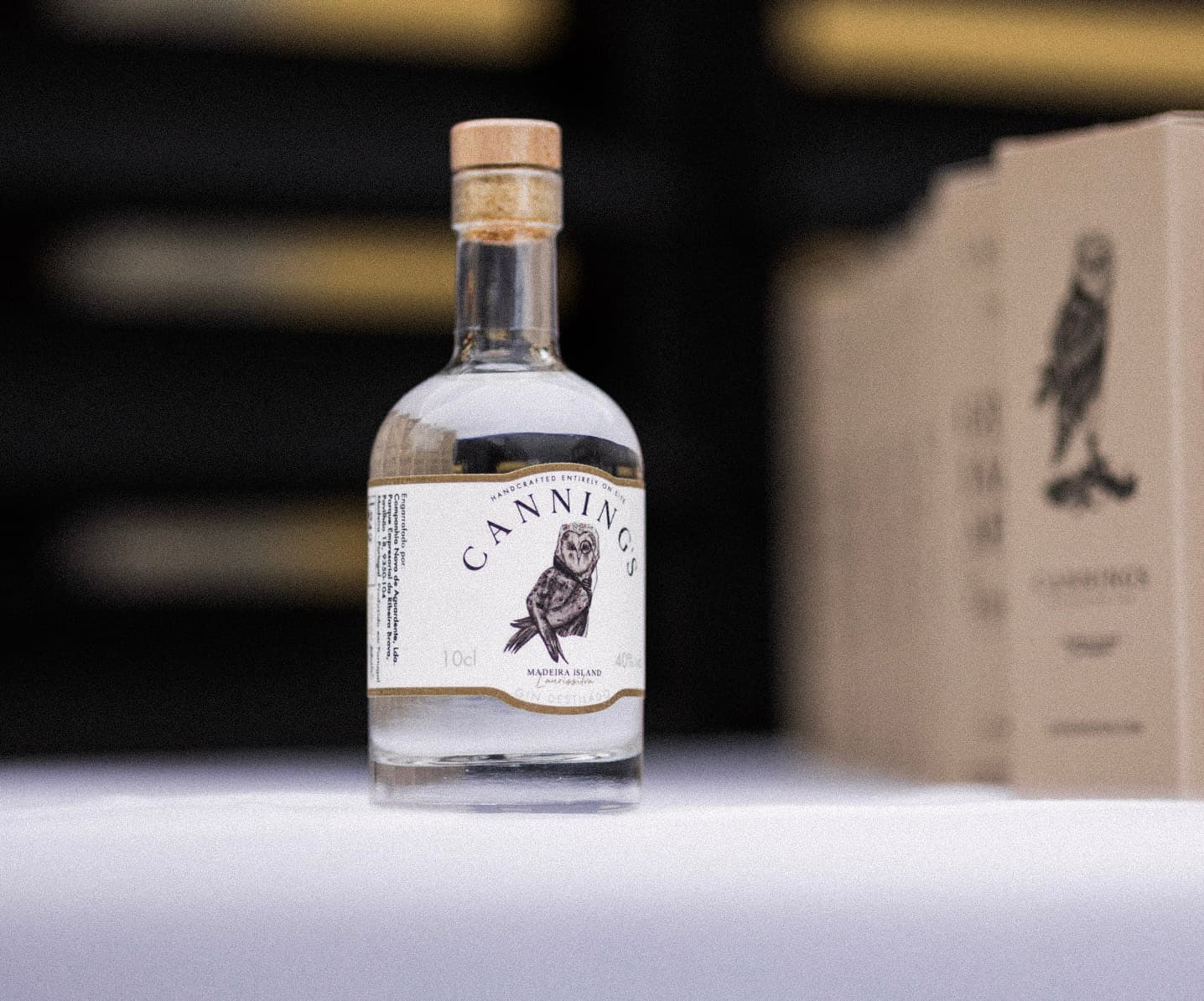 Seis garrafas de 10cl de gin Canning's na bancada da destilaria, com o alambique de cobre atrás
