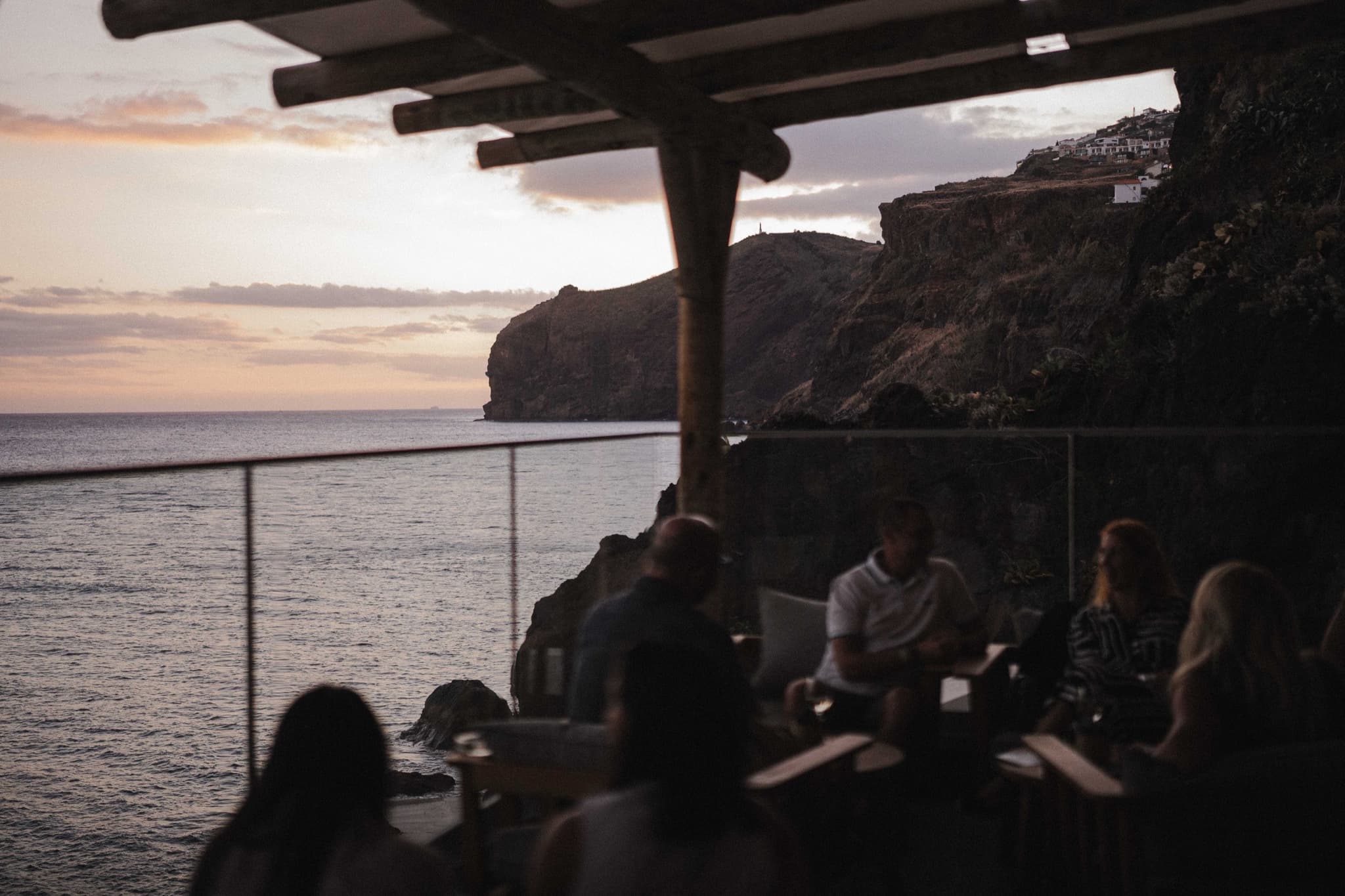 Amigos a conversar com bebidas num terraço sobre o mar ao pôr do sol